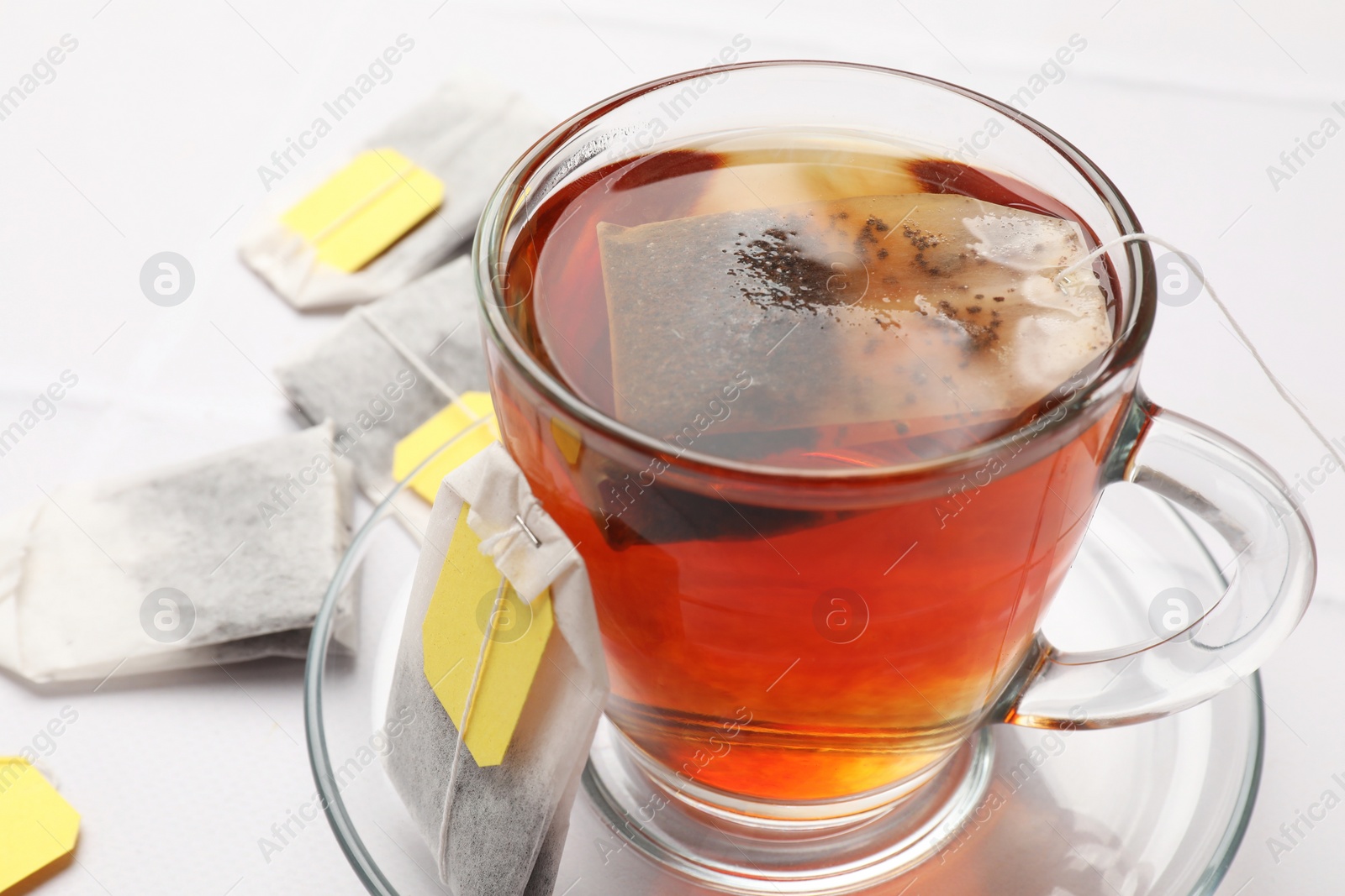 Photo of Tea bags and cup of aromatic drink on white table, closeup