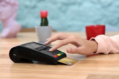 Photo of Woman using card machine for non cash payment at table, closeup