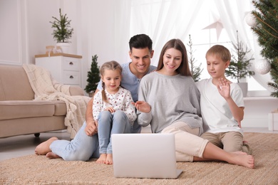 Photo of Family with children using video chat on laptop in room decorated for Christmas