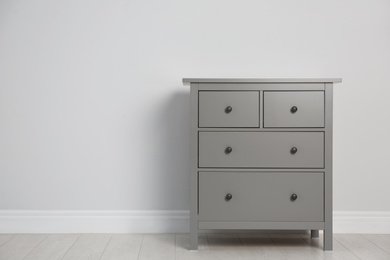 Photo of Grey chest of drawers near light wall. Space for text