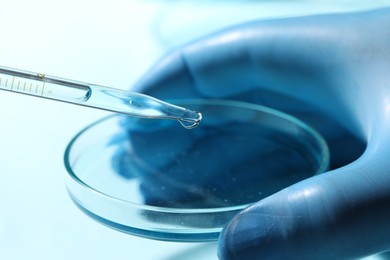 Photo of Doctor dripping liquid from pipette into petri dish on blurred background, closeup. Laboratory analysis