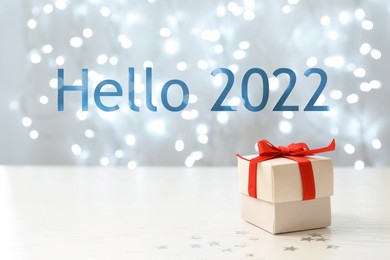 Hello 2022. Gift box on white table against blurred lights