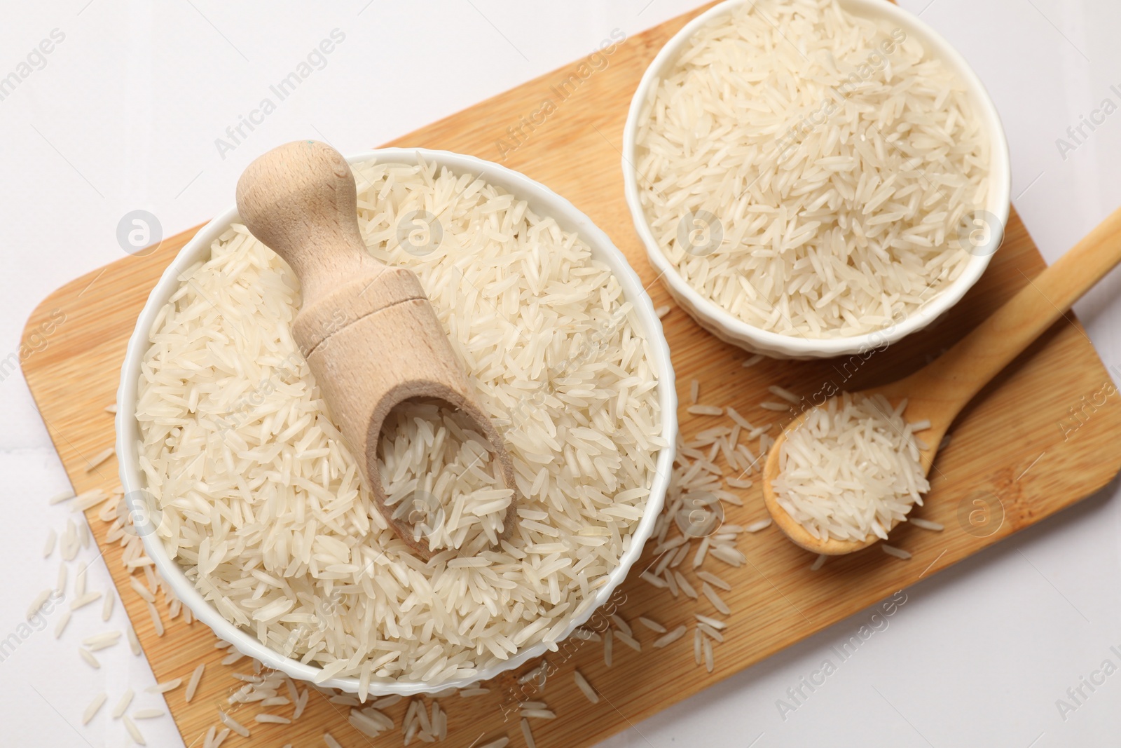 Photo of Raw basmati rice in bowl, scoop and spoon on white table, top view