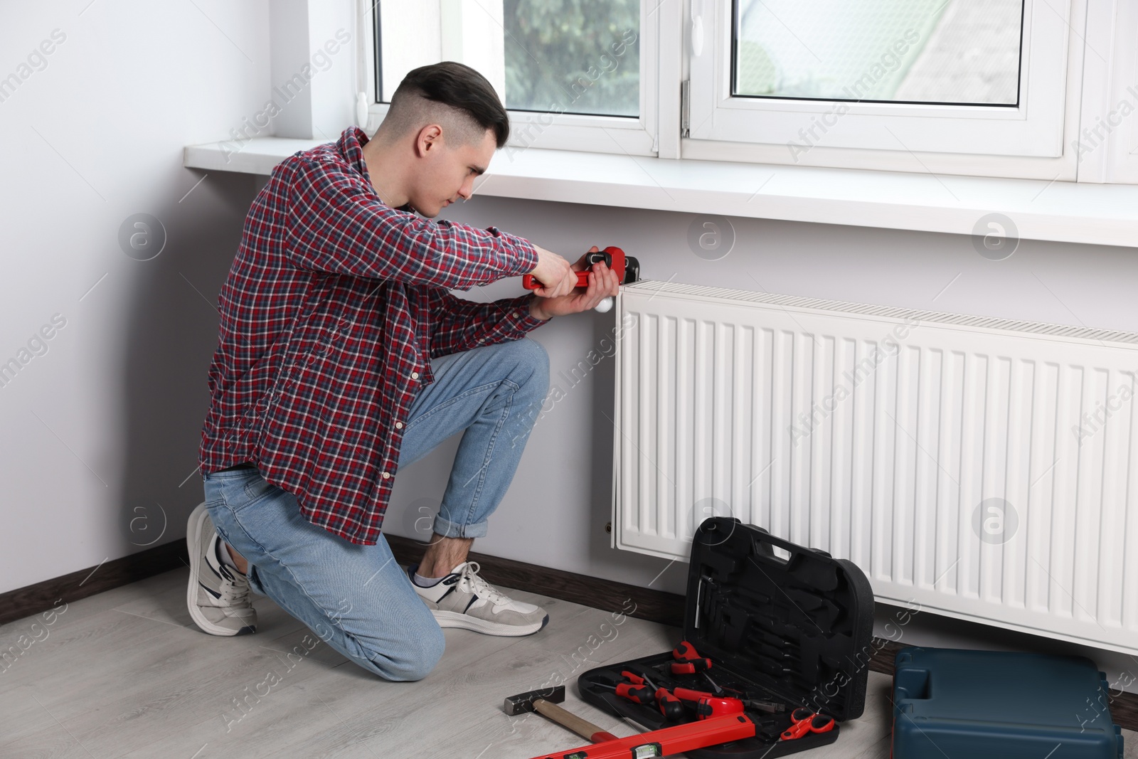 Photo of Man fixing radiator with pipe wrench in room