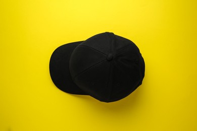 Photo of Stylish black baseball cap on yellow background, top view