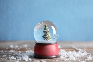 Photo of Magical snow globe with Christmas tree on wooden table against color background