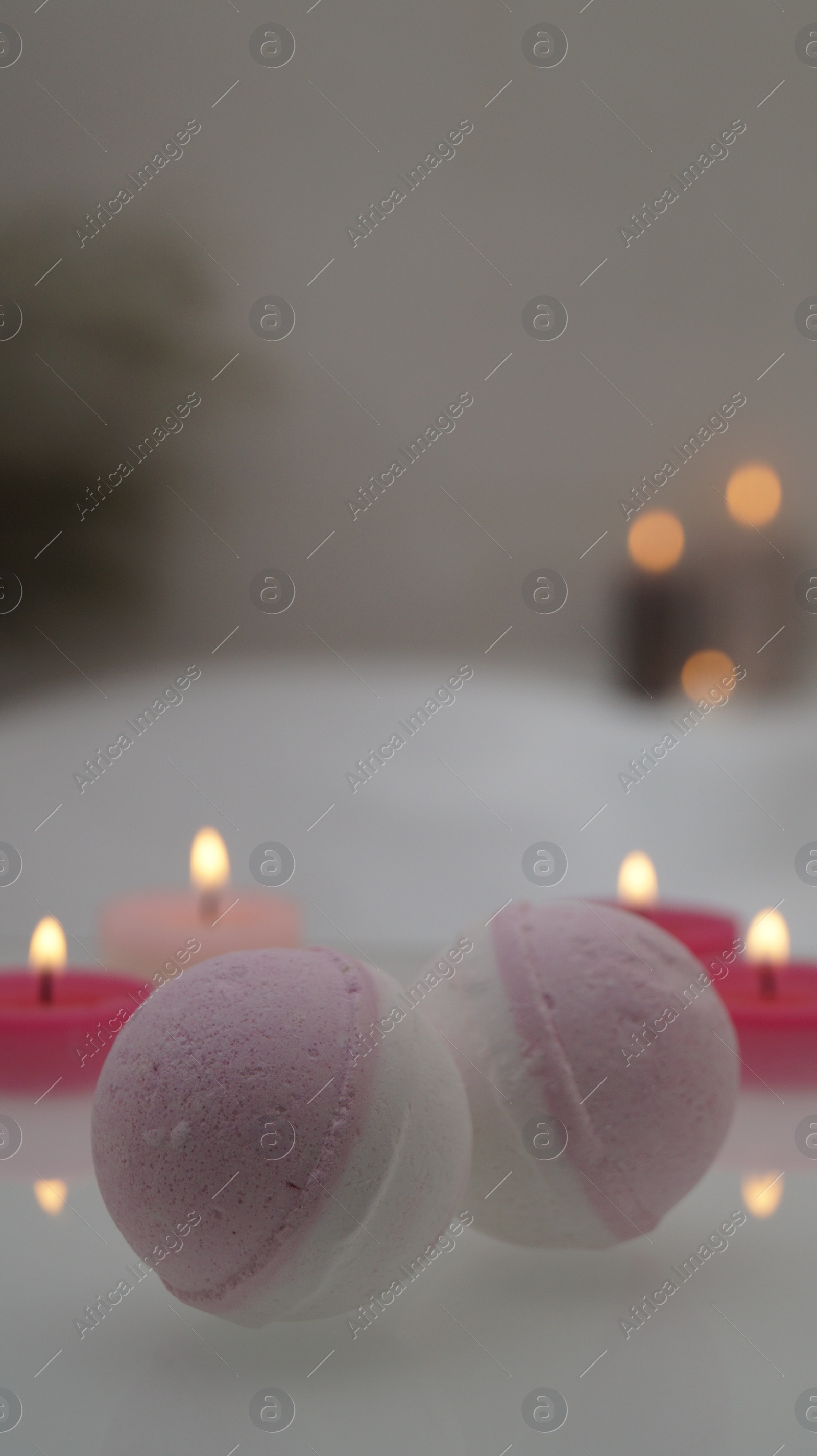 Photo of Bath bombs with burning candles on tub indoors. Bokeh effect