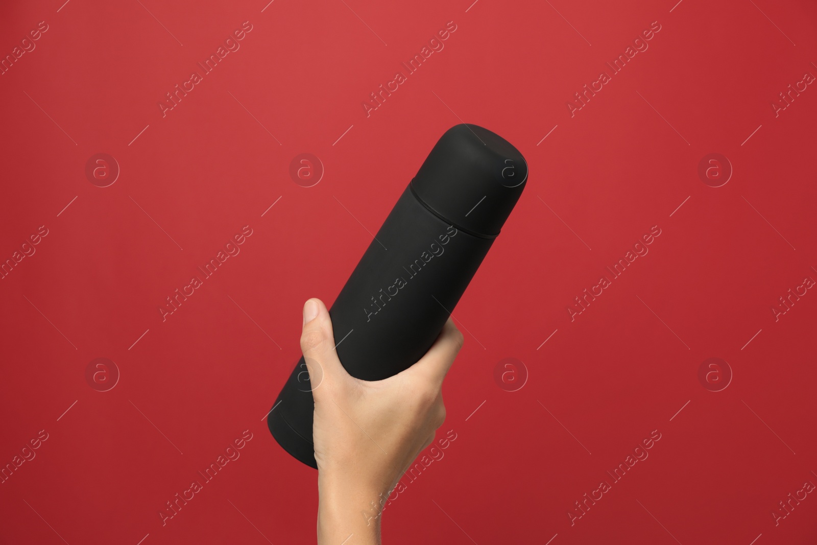 Photo of Woman holding modern black thermos on red background, closeup