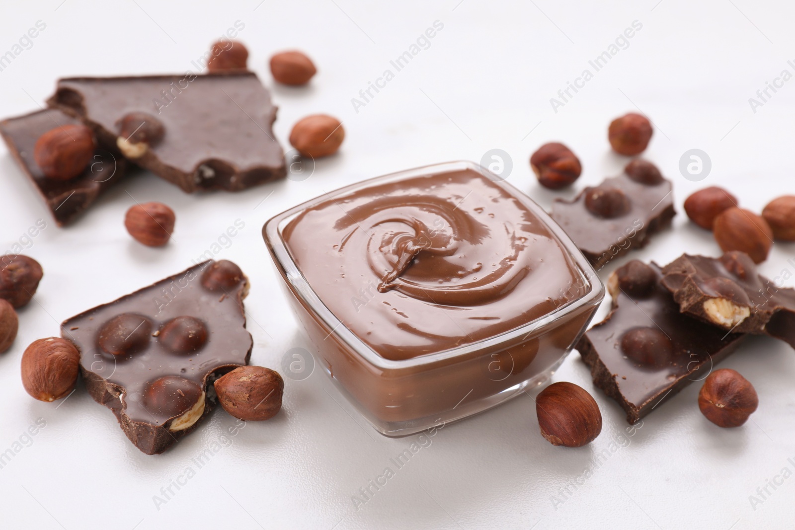 Photo of Bowl with tasty paste, chocolate pieces and nuts on white table