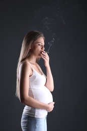 Photo of Young pregnant woman smoking cigarette on dark background. Harm to unborn baby