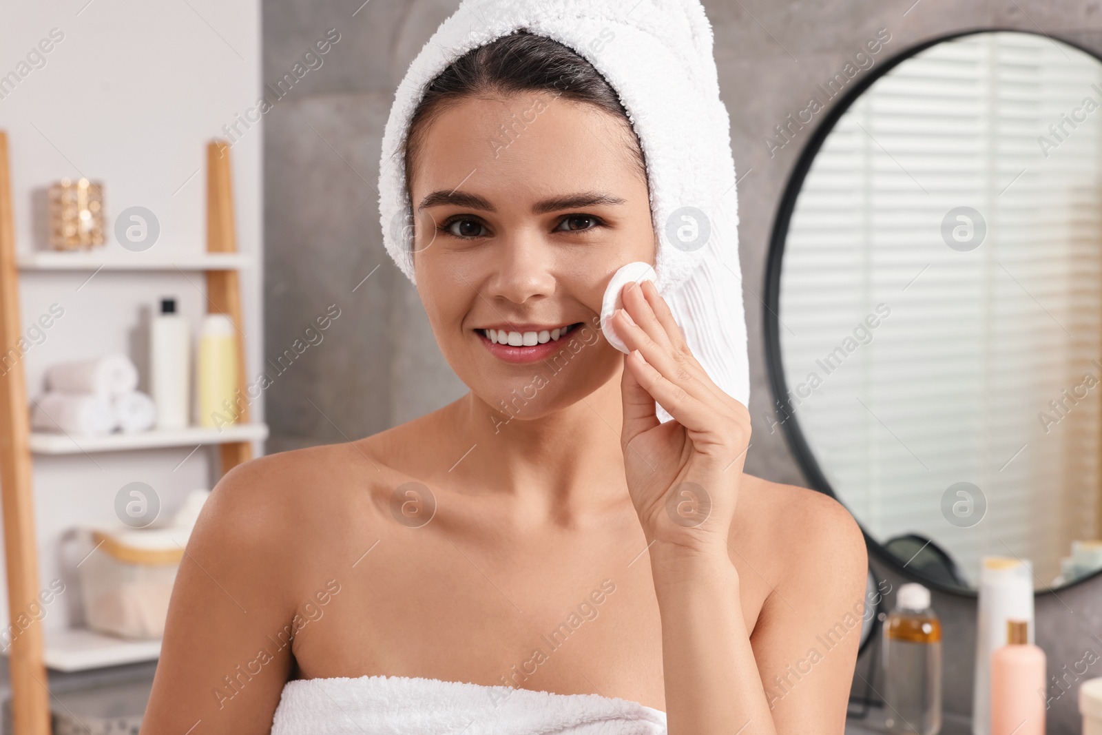 Photo of Young woman cleaning her face with cotton pad in bathroom