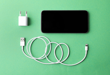 Photo of Smartphone and USB charger on green background, flat lay. Modern technology