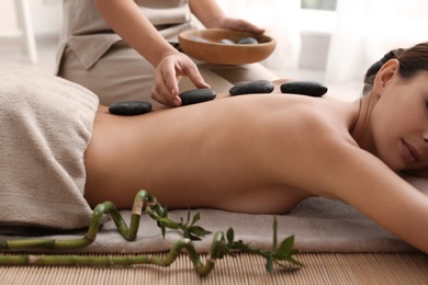 Photo of Beautiful young woman getting hot stone massage in spa salon