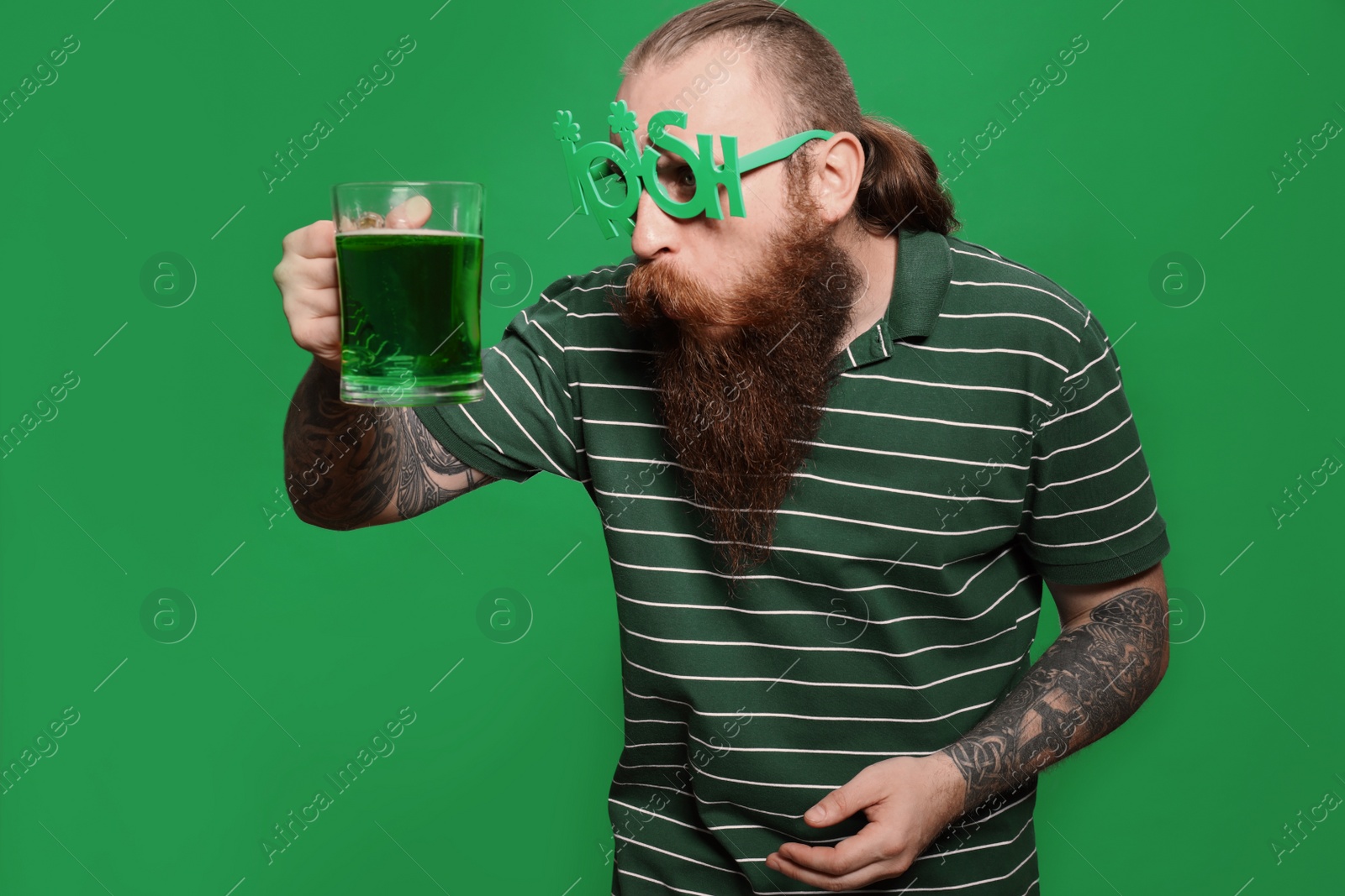 Photo of Bearded man in party glasses with green beer on color background. St. Patrick's Day celebration