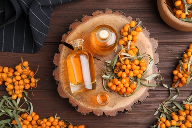 Natural sea buckthorn oil and fresh berries on wooden table, flat lay