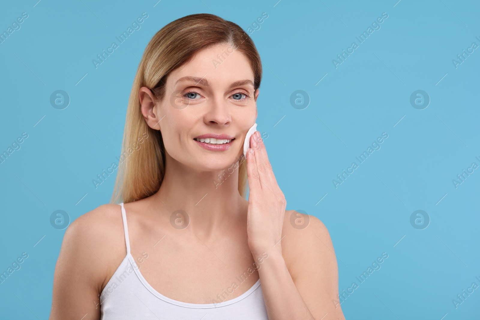 Photo of Beautiful woman removing makeup with cotton pad on light blue background, space for text