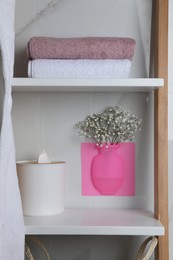 Photo of Silicone vase with flowers on white marble wall and shelving unit in stylish bathroom