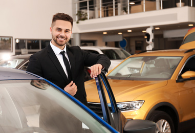 Young salesman near new car in dealership