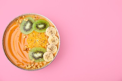 Bowl of delicious fruit smoothie with fresh banana, kiwi slices and granola on pink background, top view. Space for text