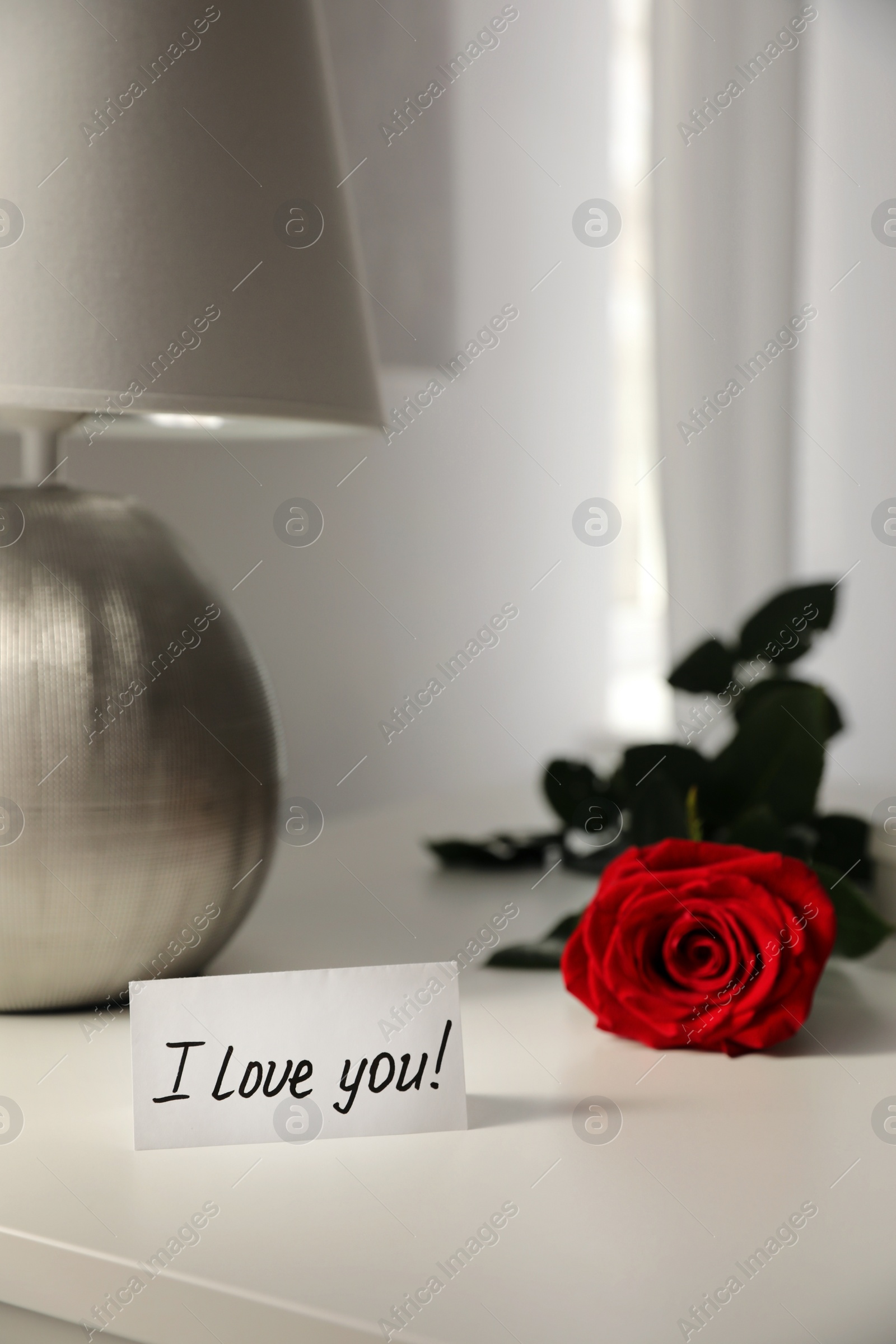 Photo of Paper with text I Love You and red rose on table indoors