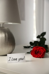 Paper with text I Love You and red rose on table indoors