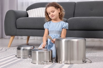 Photo of Little girl pretending to play drums on pots at home