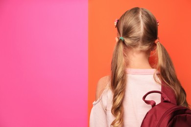 Photo of Cute little girl with backpack on colorful background, back view. Space for text