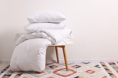 Soft pillows and duvet on side table near light wall indoors, space for text