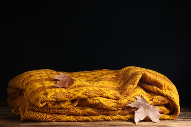 Orange knitted plaid with dry leaves on wooden table. Space for text