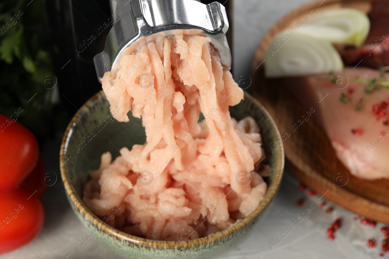 Photo of Electric meat grinder with chicken mince and products on grey table, closeup