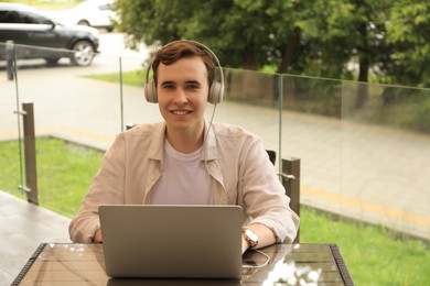Handsome young man with headphones working on laptop in outdoor cafe