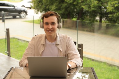 Photo of Handsome young man with headphones working on laptop in outdoor cafe