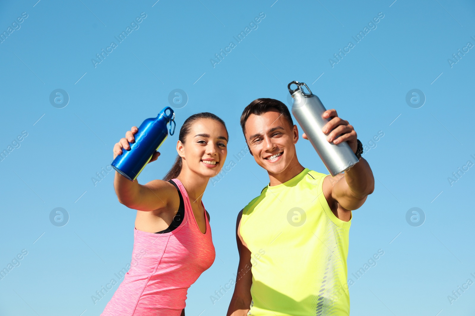 Photo of Young sporty couple with water bottles against blue sky on sunny day
