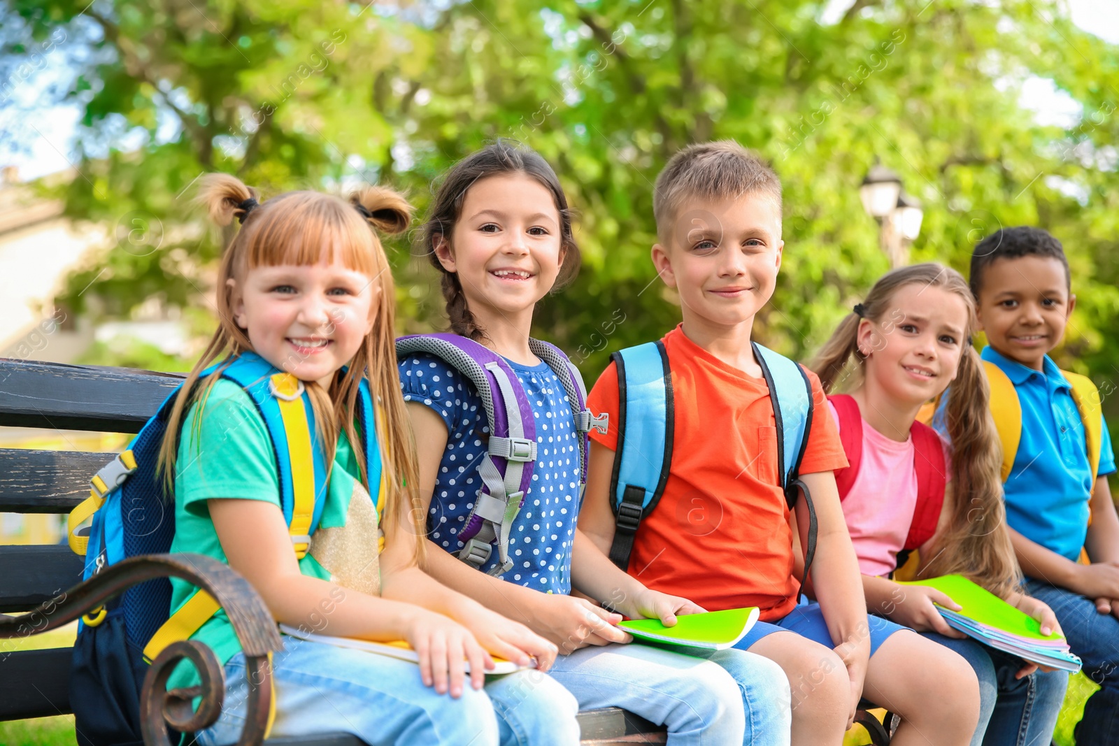 Photo of Cute little children with backpacks and notebooks outdoors. Elementary school