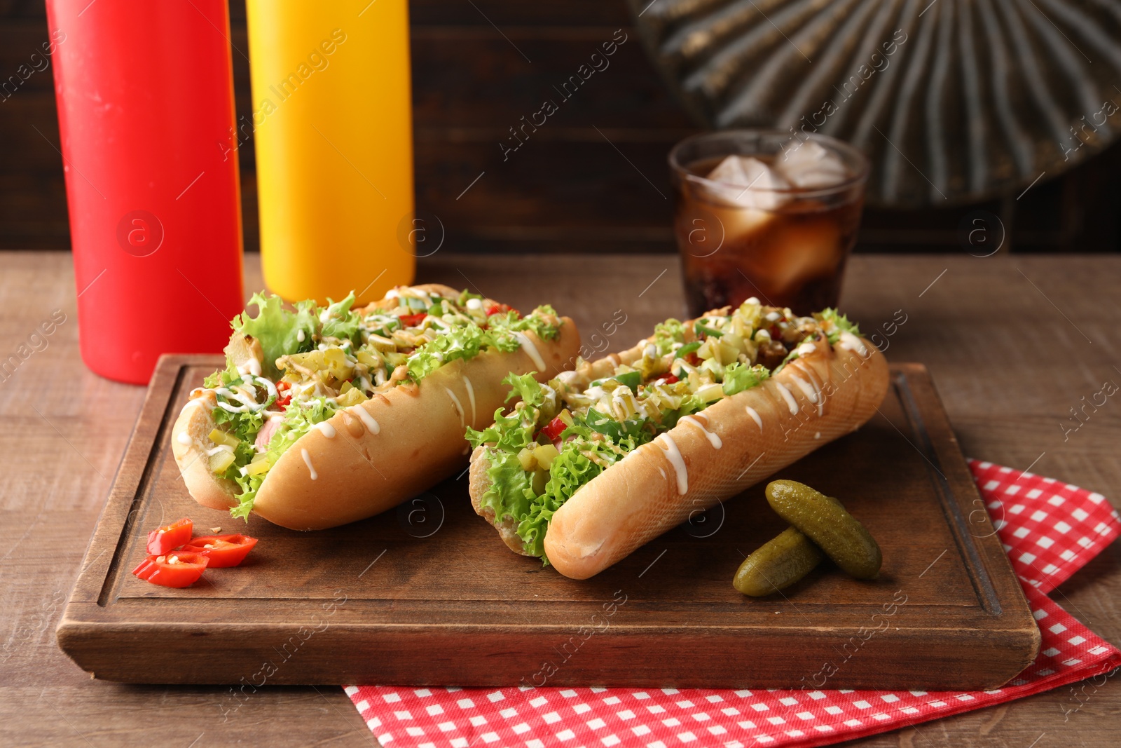 Photo of Tasty hot dogs with chili, lettuce, pickles and sauces on wooden table, closeup