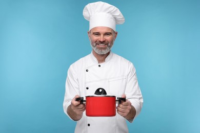 Photo of Happy chef in uniform with cooking pot on light blue background