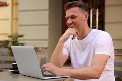 Photo of Handsome man working on laptop at table in outdoor cafe