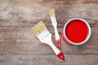 Tin can with paint and brushes on wooden background, top view