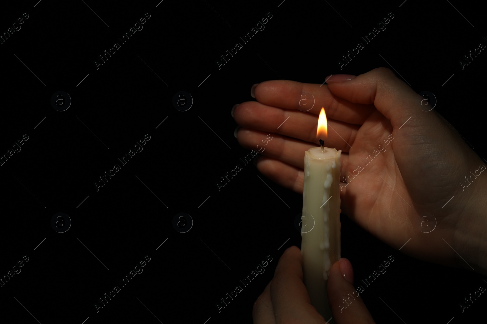 Photo of Woman holding burning candle in hands on black background, closeup. Space for text