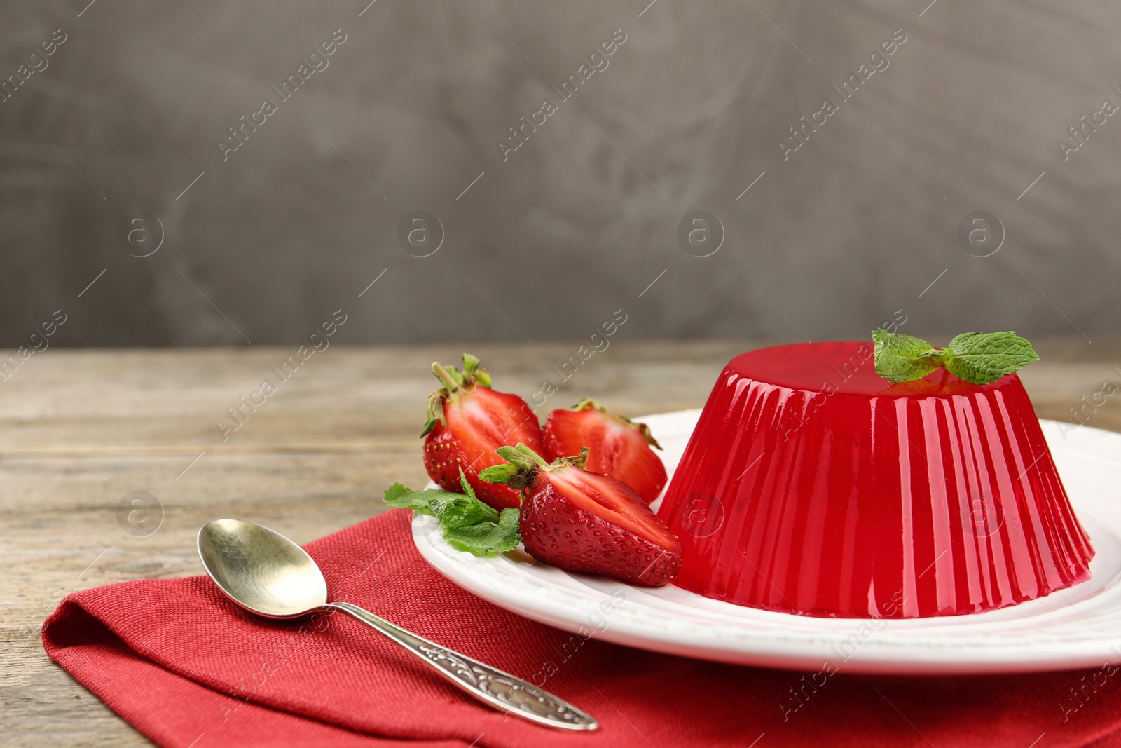 Photo of Plate of tasty strawberry jelly served on wooden table, space for text
