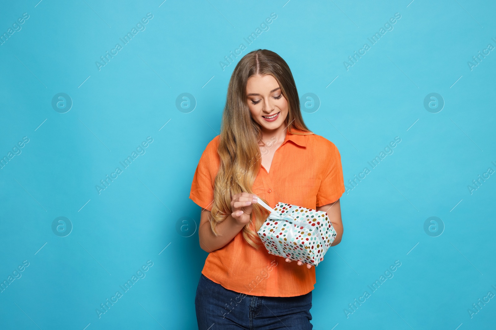 Photo of Beautiful young woman holding colorful gift box on light blue background