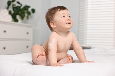 Cute little baby with moisturizing cream onto body sitting on bed at home