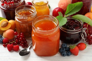 Photo of Jars with different jams and fresh fruits on white wooden table