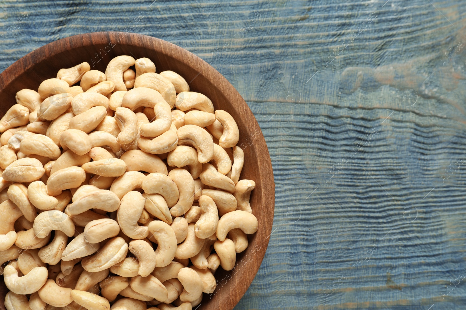 Photo of Tasty cashew nuts in bowl on wooden table, top view. Space for text