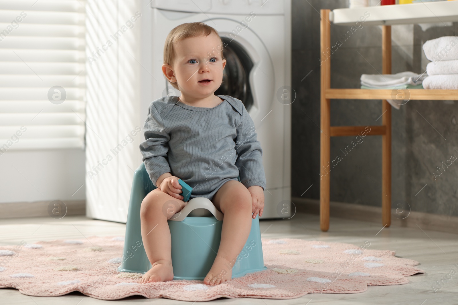 Photo of Little child sitting on plastic baby potty indoors. Space for text