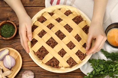 Photo of Woman making lattice top for meat pie at wooden table, top view