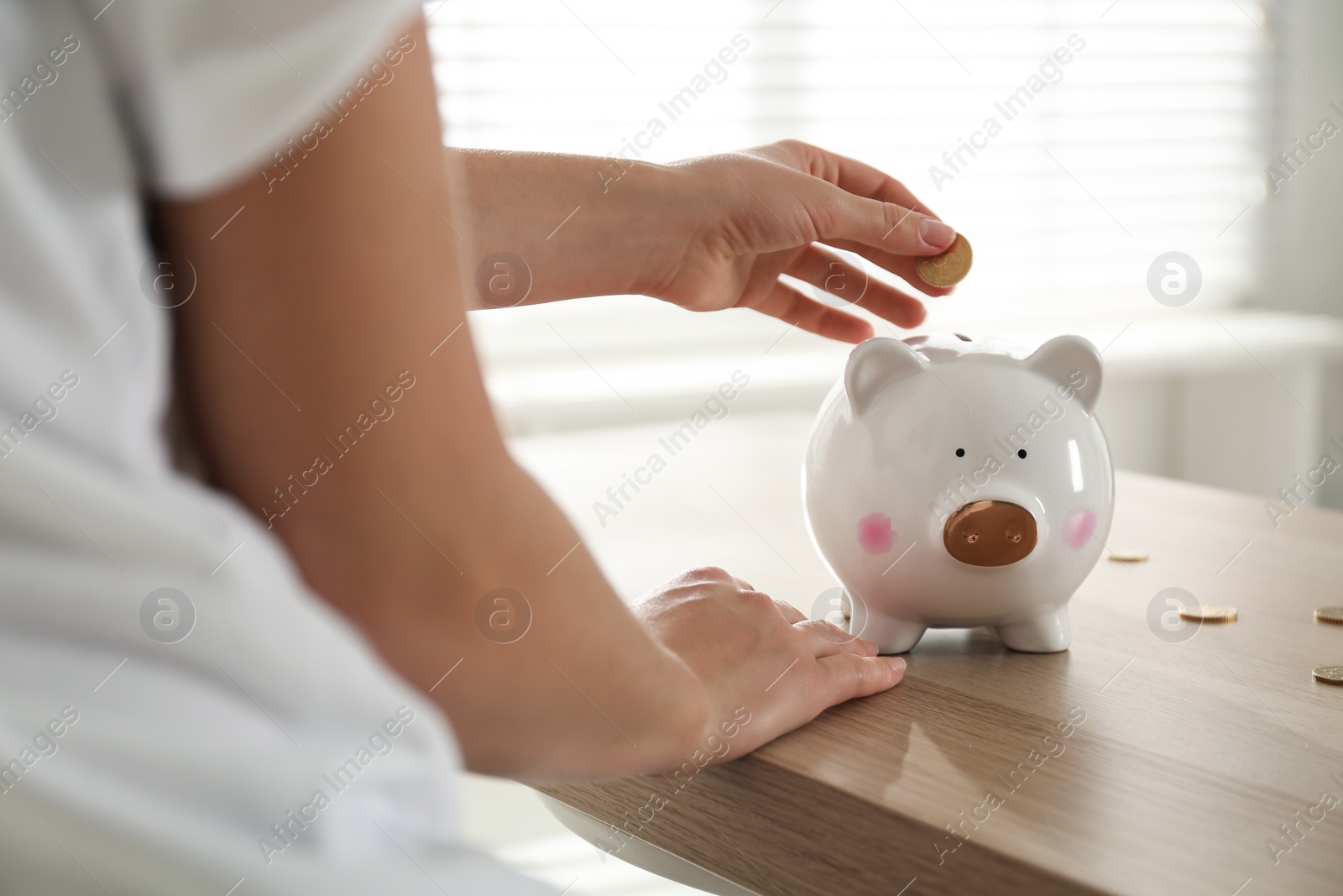 Photo of Woman putting money into piggy bank at wooden table indoors, closeup