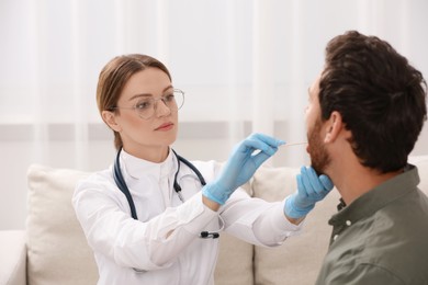 Photo of Doctor examining man`s oral cavity with tongue depressor indoors
