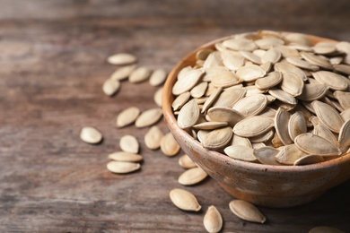 Photo of Full bowl of raw pumpkin seeds on wooden background