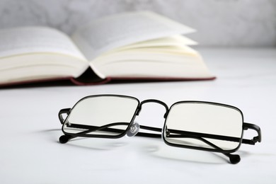 Photo of Glasses in stylish frame on white table, space for text